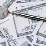 A stack of bills and a dental instrument represent the costs of dental care.