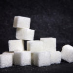 Cubes of sugar against a black background symbolize the dire effects of this substance on the health of diabetics and their teeth.