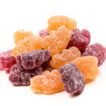 A pile of colorful gummy candies coated in sugar, featuring shapes that resemble bears. The candies are in shades of purple, orange, and red, arranged against a plain white background.