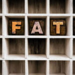 Rustic metal letters spelling out the word "FATE" are placed in separate compartments of a white wooden cubby shelf. The background of the shelf is textured, giving a sense of depth and the letters show a vintage, weathered look, creating a philosophical or reflective mood.